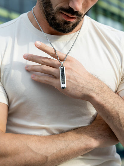 Silver pendant necklace worn by man, black-studded pendant centered on chain