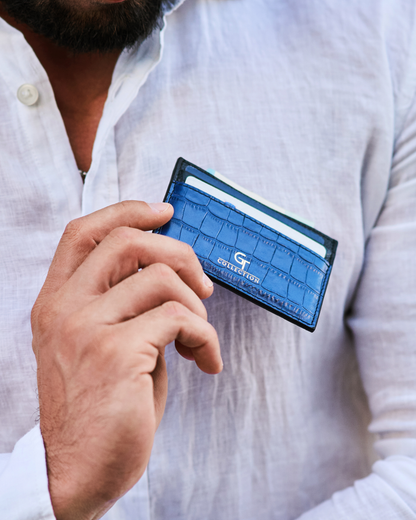Blue croc-embossed leather card holder held with front logo facing outward.