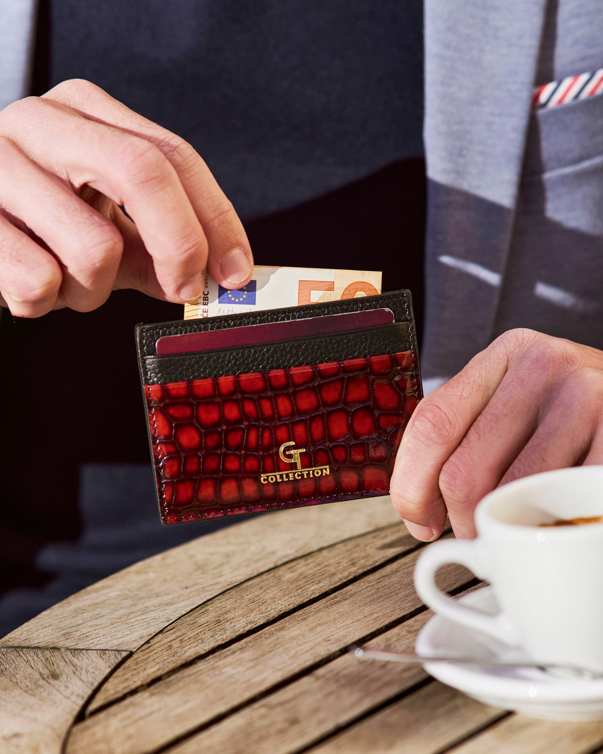 Red croc-embossed leather card holder with gold logo, held open on a table.
