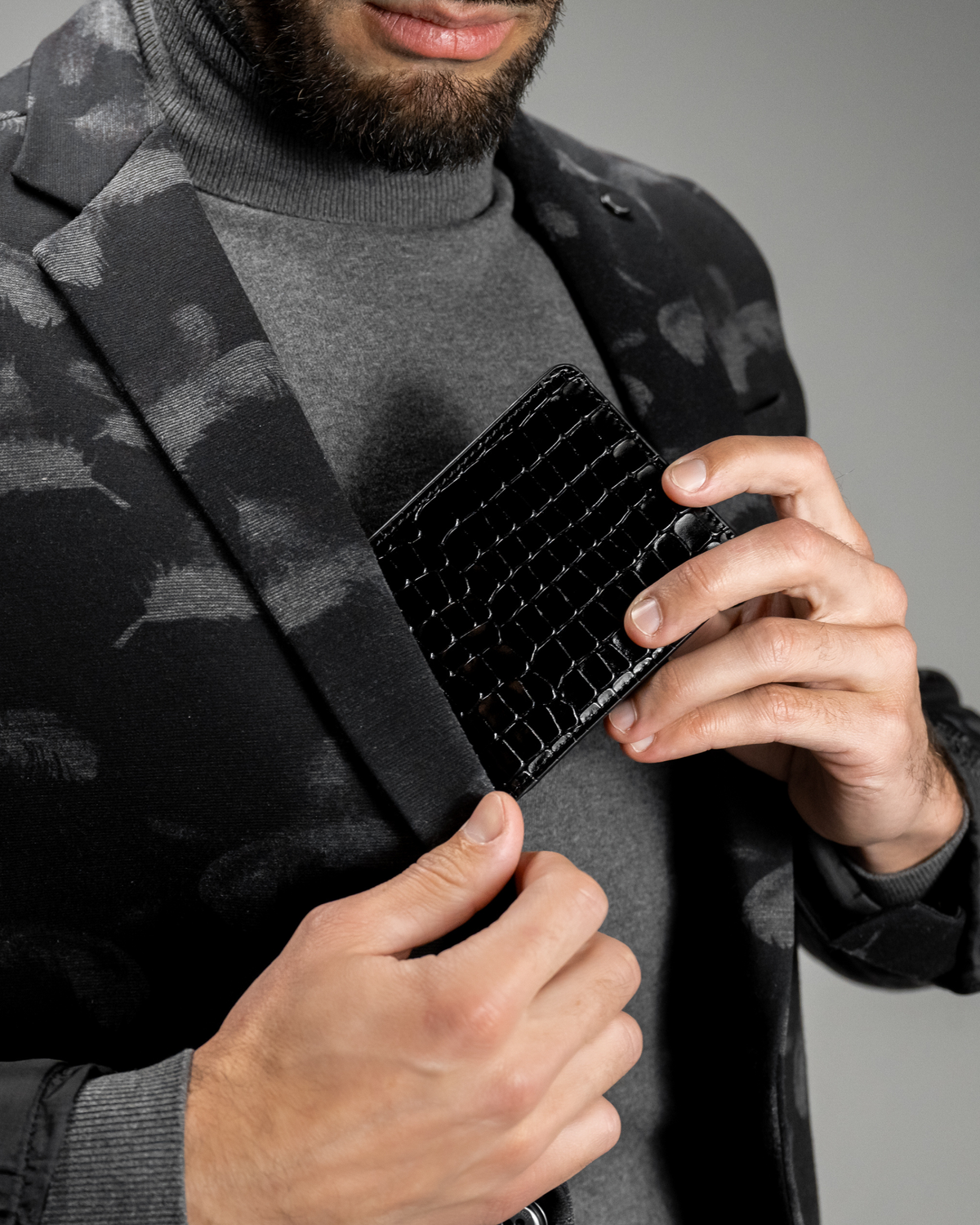 Black croc-embossed leather wallet with slim fold, held in hand.