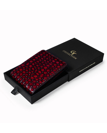 Red croc-embossed leather wallet with logo on card slot, shown beside black box.
